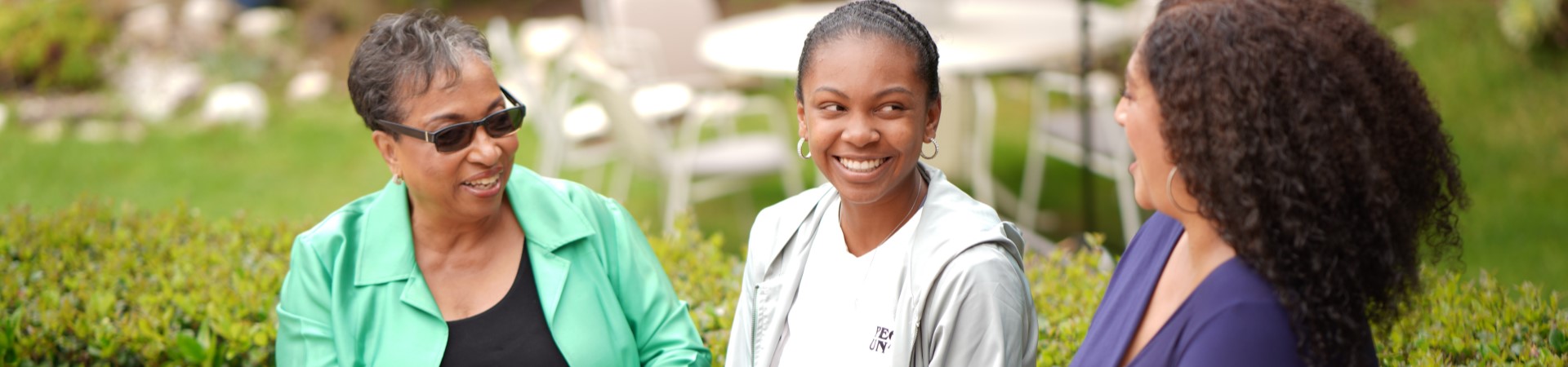  an adult Black woman, a teenaged Black girl, and a Black adult woman sitting in a row, smiling and talking 